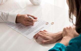 Two people sit at a table with one person signing a divorce agreement form, guided by the divorce laws of Suwanee, GA. Two wedding rings are placed on the table beside the document.