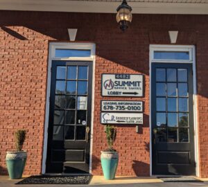 Two black double doors on a red brick building, labeled as Summit Office Suites and Family Law PC, with potted plants and business signs displaying contact information.